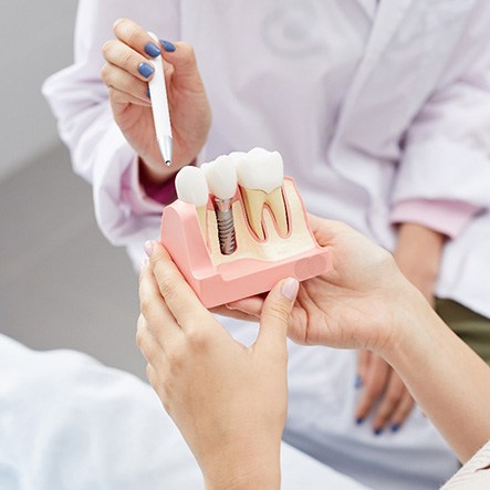 Dentist pointing to sample implant held by patient