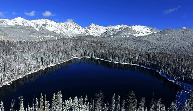 Aerial view of lake surrounded by snowy forest and mountains