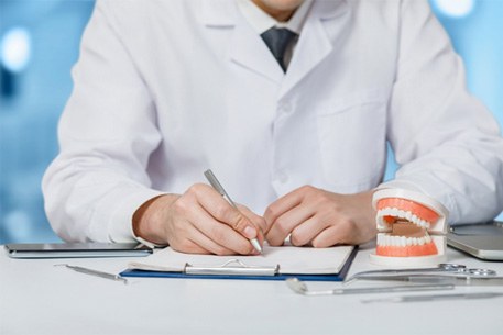 a dentist writing on a clipboard with a model of a mouth sitting next to them
