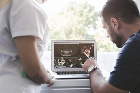 a dentist and a dental assistant looking at X-rays on a computer monitor