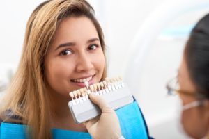 dentist holding a row of veneers to a patient’s smile 