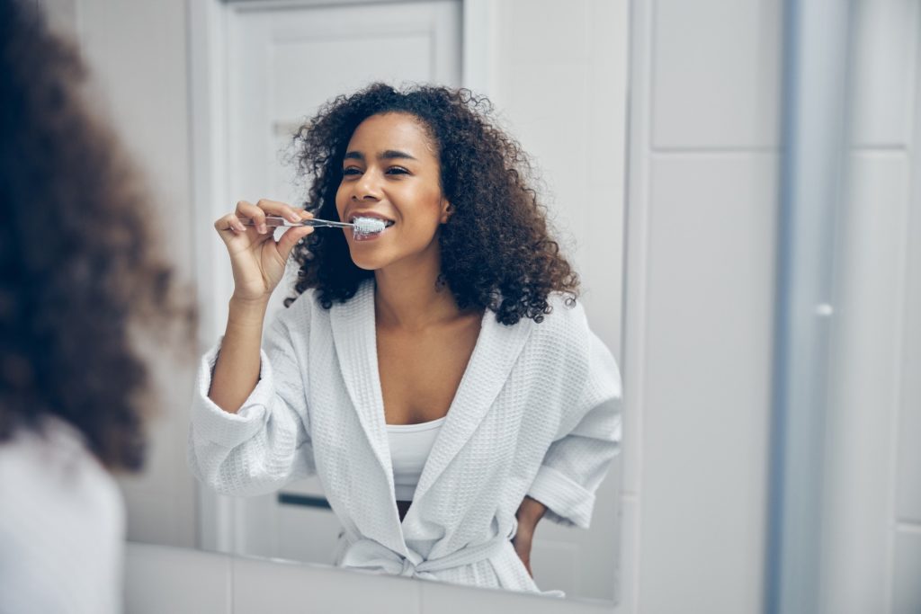 Young woman in white robe brushing her teeth