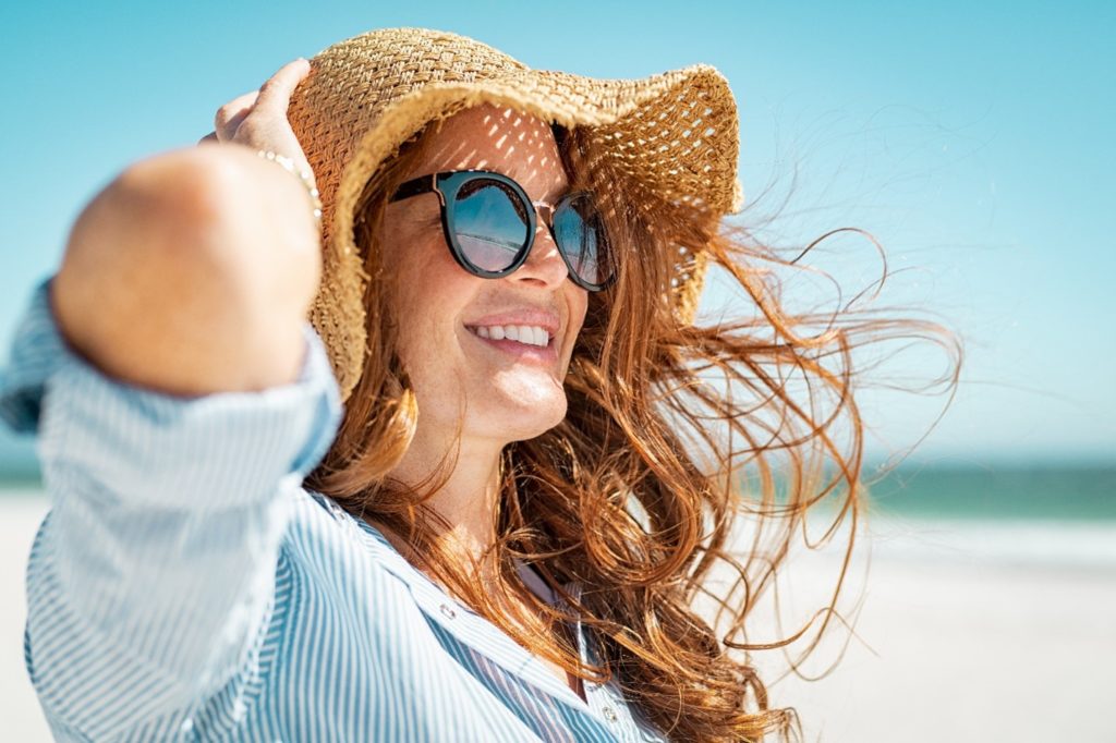 Smiling woman holding her hat while walking on beach